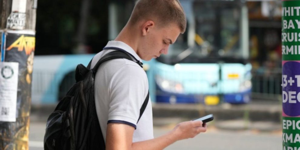 File photo of a youth using his phone while waiting to cross the street in Sydney, Dec. 8, 2025.