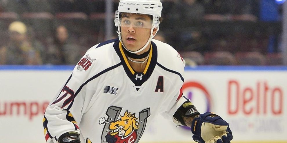 Barrie Colts defenceman Kashawn Aitcheson skating with the puck during an OHL game, wearing his team uniform and helmet, focused on play.