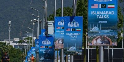 Workers walk past billboards near the Serena Hotel in Islamabad ahead of U.S.-Iran negotiations