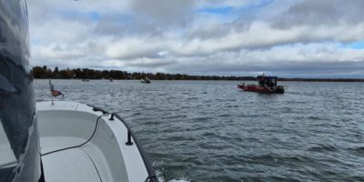 First responders assist a boater aboard a partially submerged vessel on Lake Couchiching